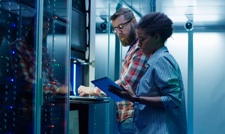 Man and woman with tablet using laptop in server room while checking servers